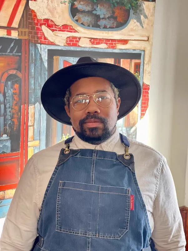 Chef KJ Bradford in a dark wide-brimmed hat and blue apron