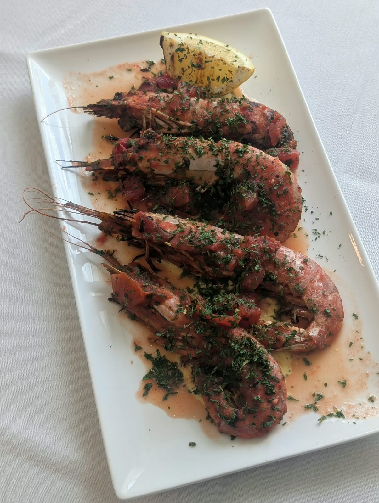 Grilled head-on shrimp in tomato and herb sauce with a lemon wedge