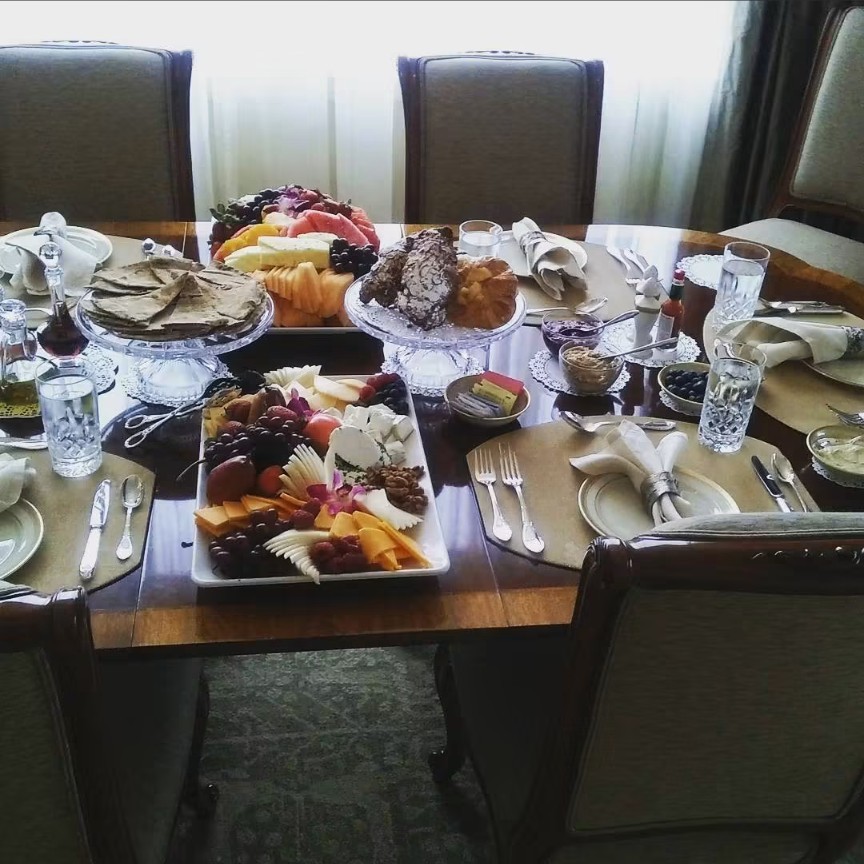 A dining table set with crystal glasses, fruit and cheese platters, flatbread and pastries